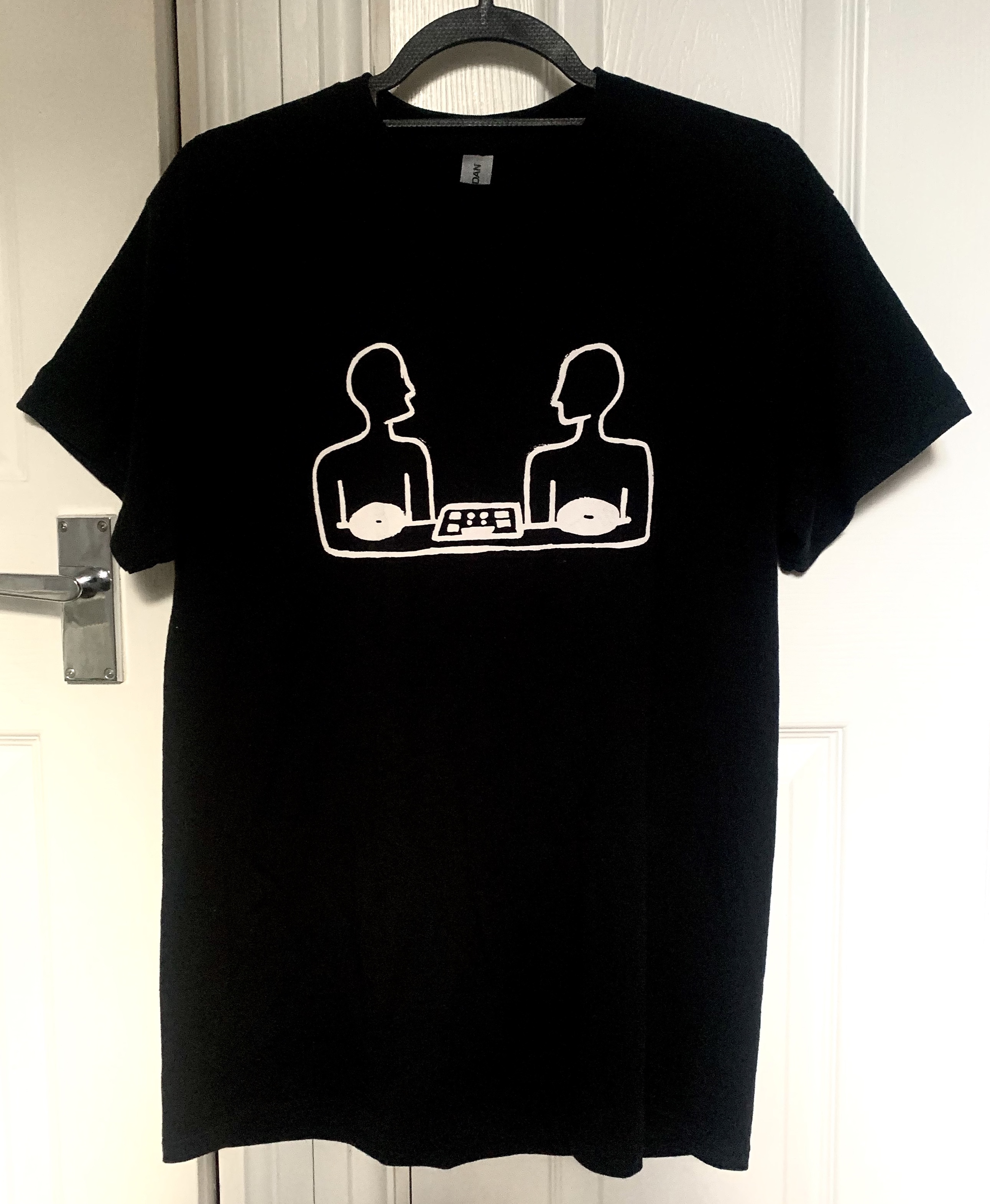 Photo of the EFS T-Shirt, a black t-shirt with a white line drawing graphic of two people sitting beside a mixing deck.