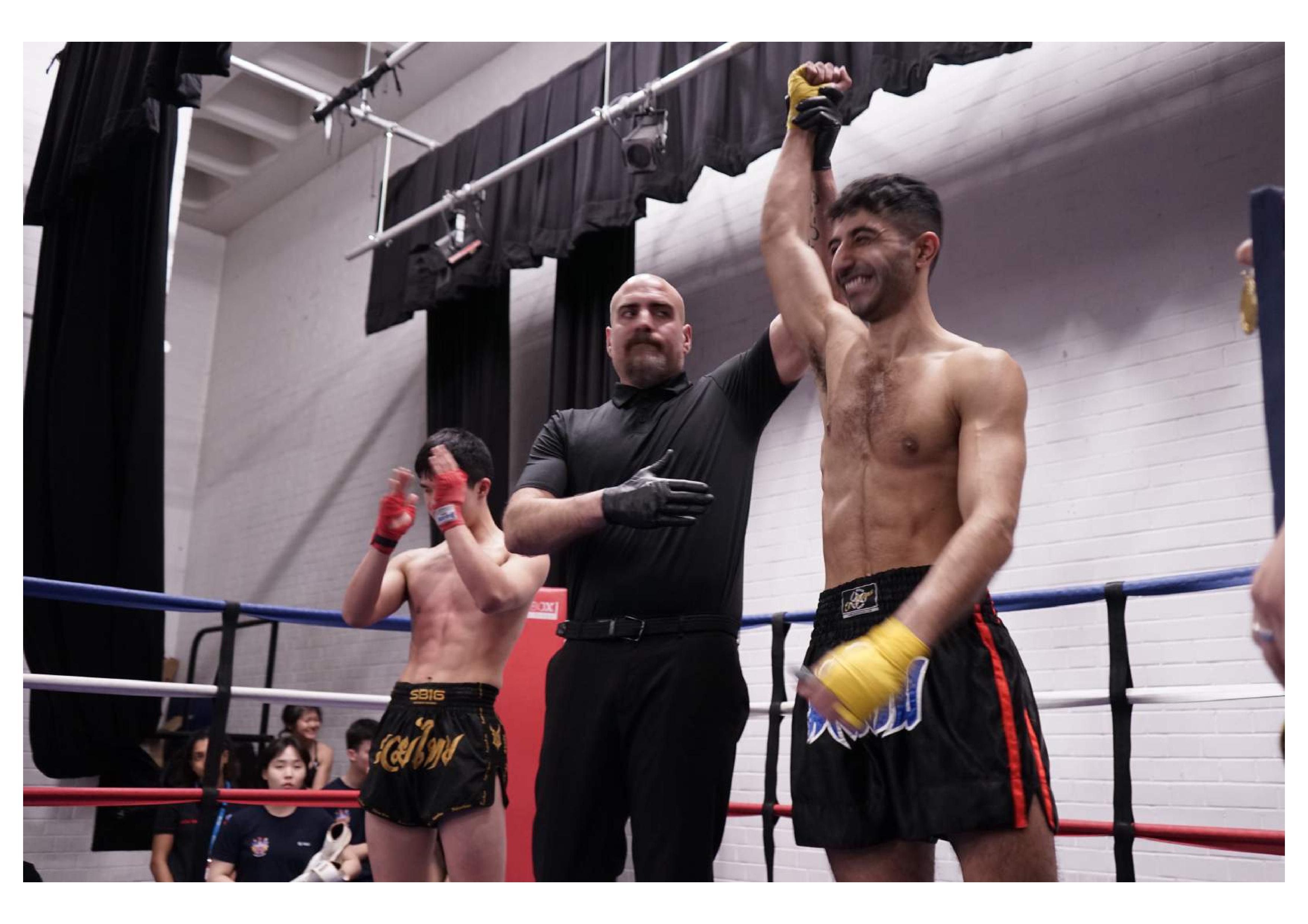 Male fighter with hand raised in a boxing ring after a fight next to referee and opponenet