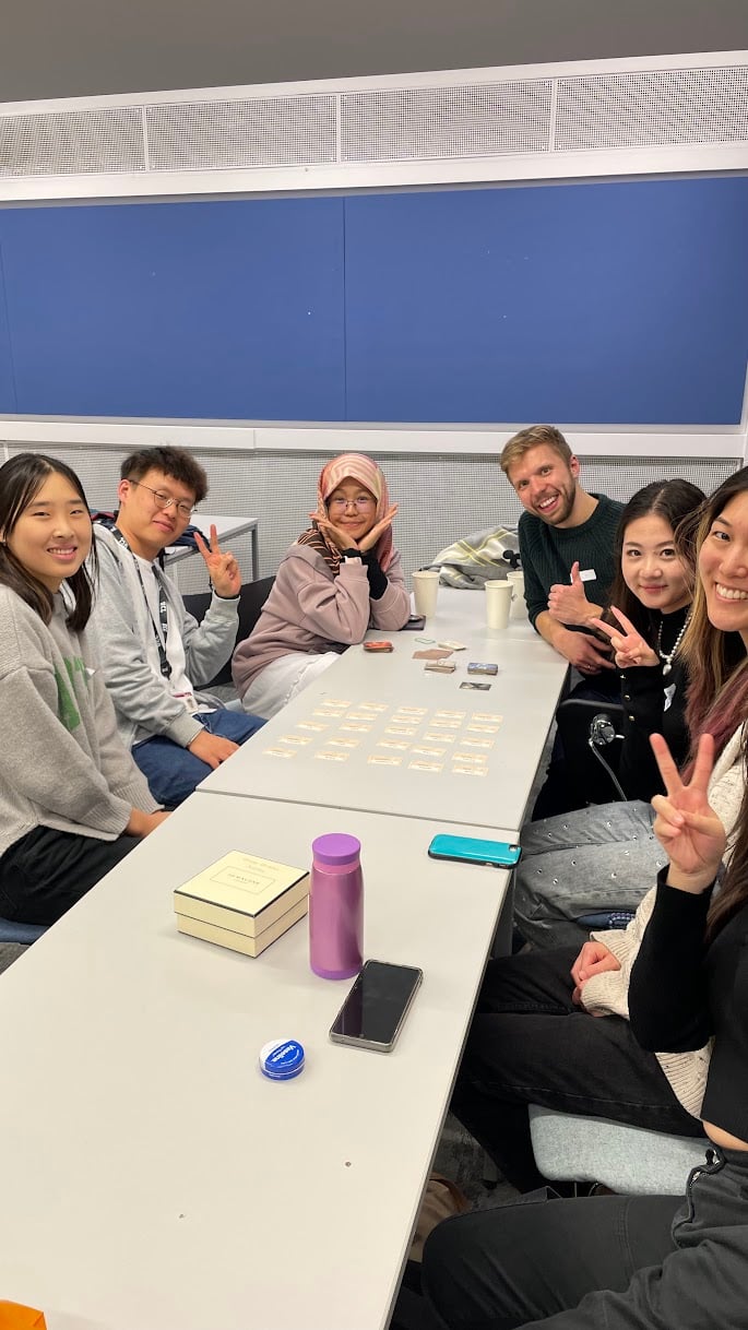 Members at a previous Giving Voice social event, sat around a table, smiling