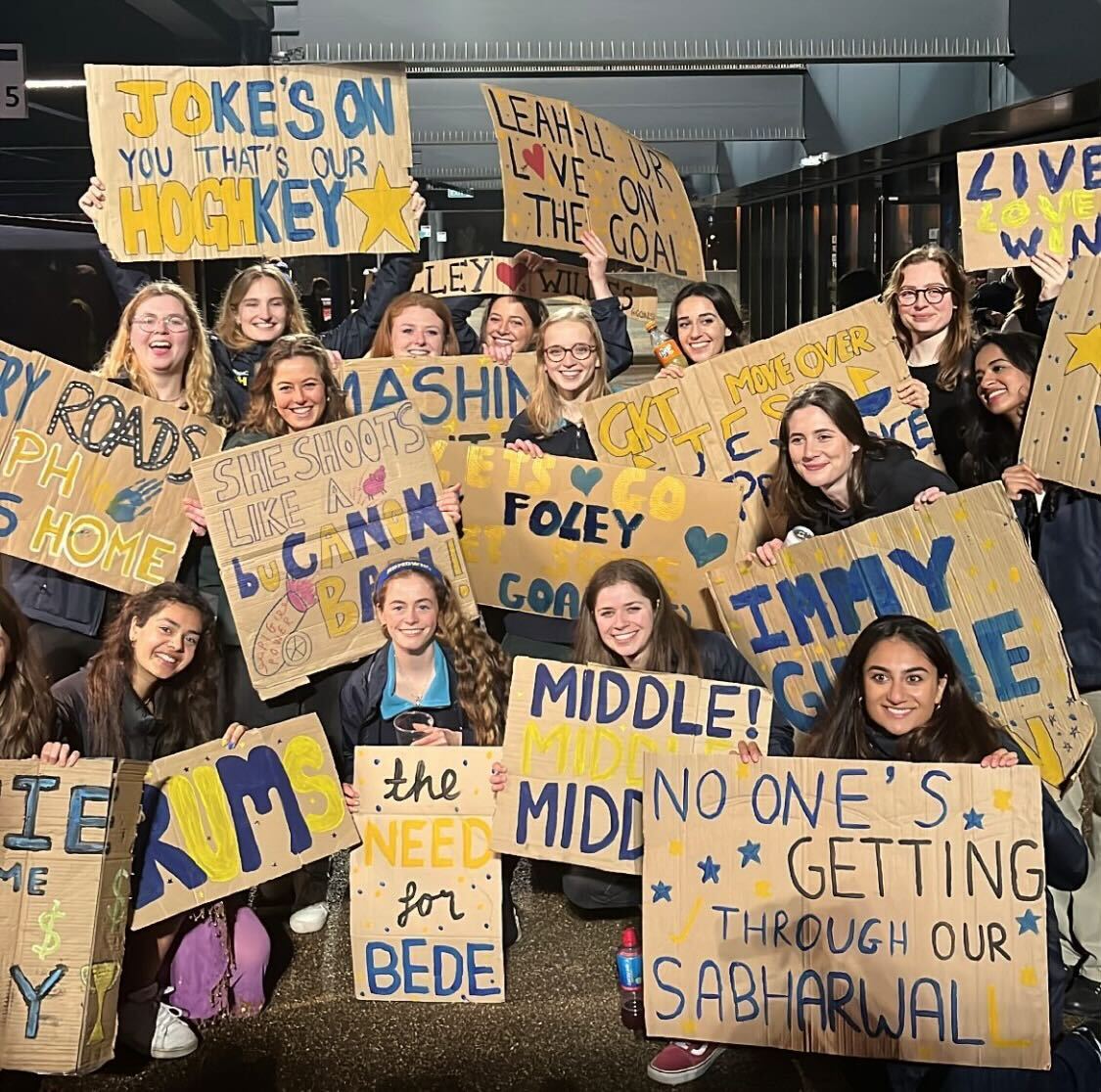 RUMS Women's Hockey crowd with signs at the match, including
'Jokes on you that's our Hoghkey'
'Leah-ll ur love on the goal'
'The need for Bede'