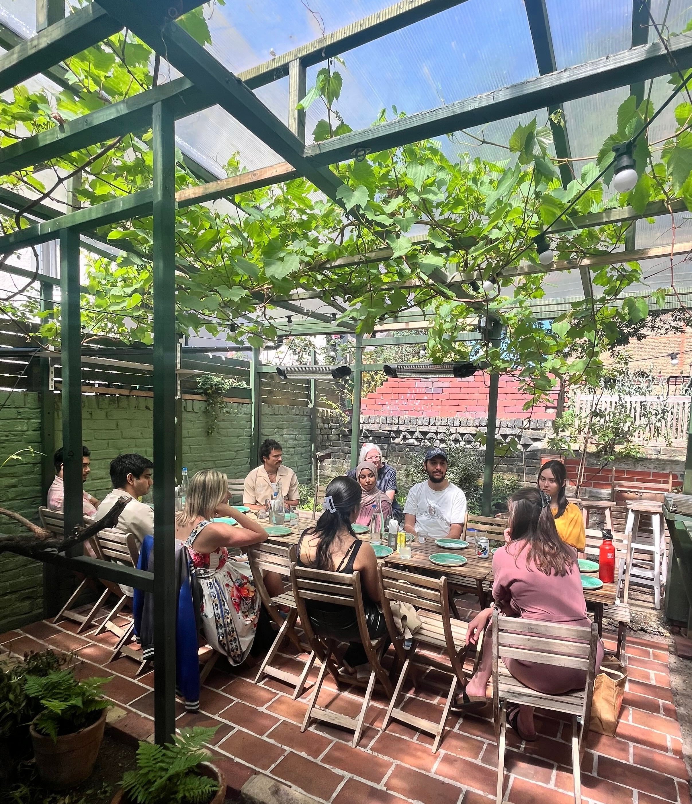 Students and staff sitting together around a table having a discussion while enjoying a meal in a garden