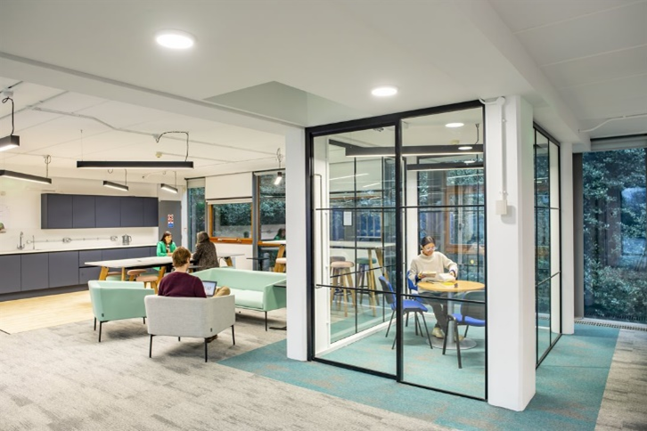 Modern study space with a glass meeting room enclosed within an open plan study space with sofas and tables