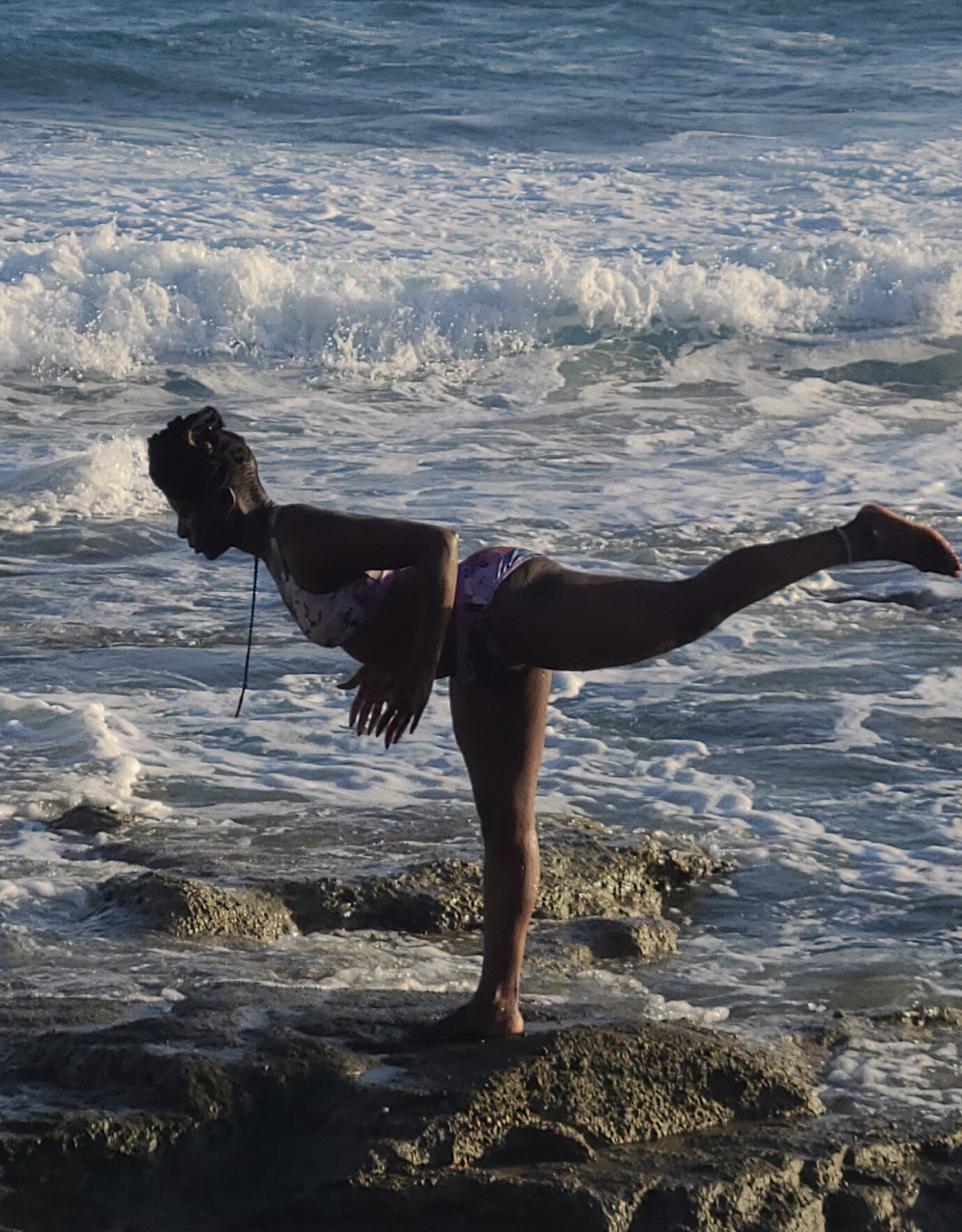 Yoga teacher Sima performing warrior 3 pose on a rock by the sea.