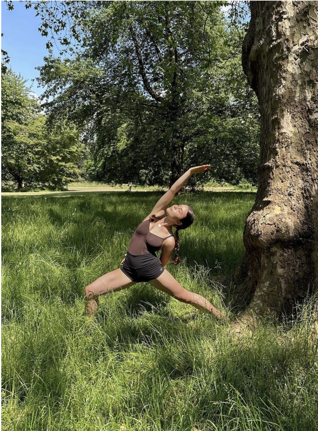 Yoga teacher Helena performing a reversed warrior pose in long grass by a tree.