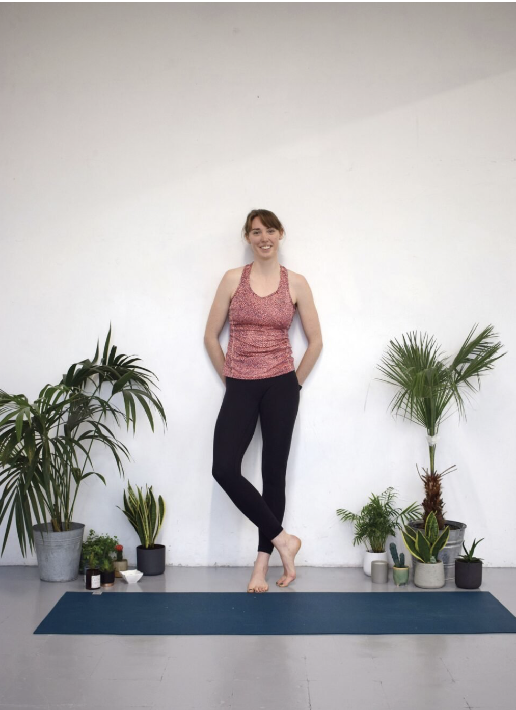 Yoga teacher Rosie stood on her mat with potted plants decorating the space