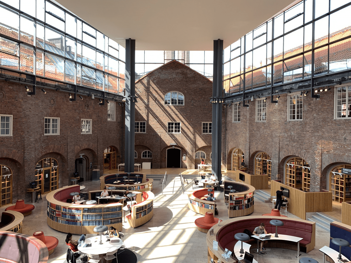 A large study space with exposed brick walls, high ceilings, and circular booths with tables and chairs