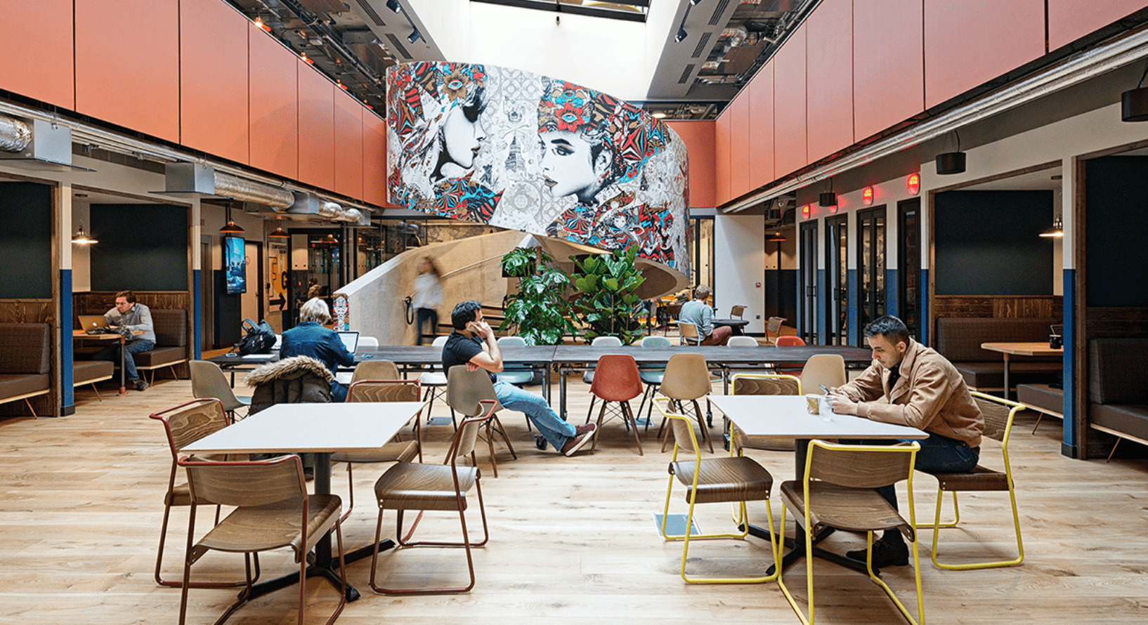 A modern study space with a feature mural on a spiral staircase, and several desks of varying size with study booths on the side of the space