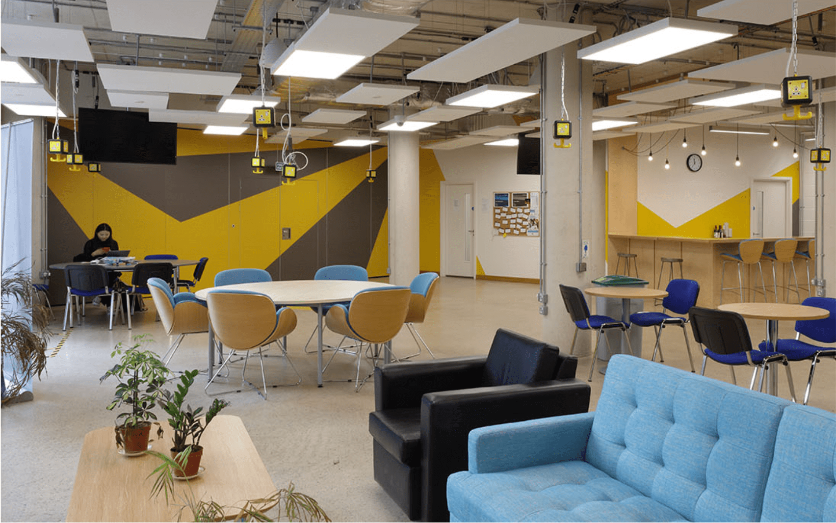 A modern study space with sofas, a yellow and grey feature wall, and round tables of varying size
