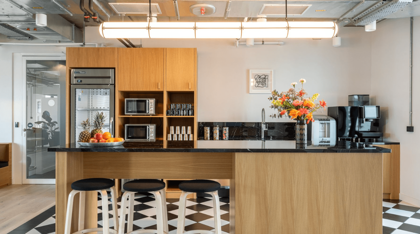 Kitchen facility in a shared study space with microwaves, a fridge, a sink, and a breakfast bar with stools