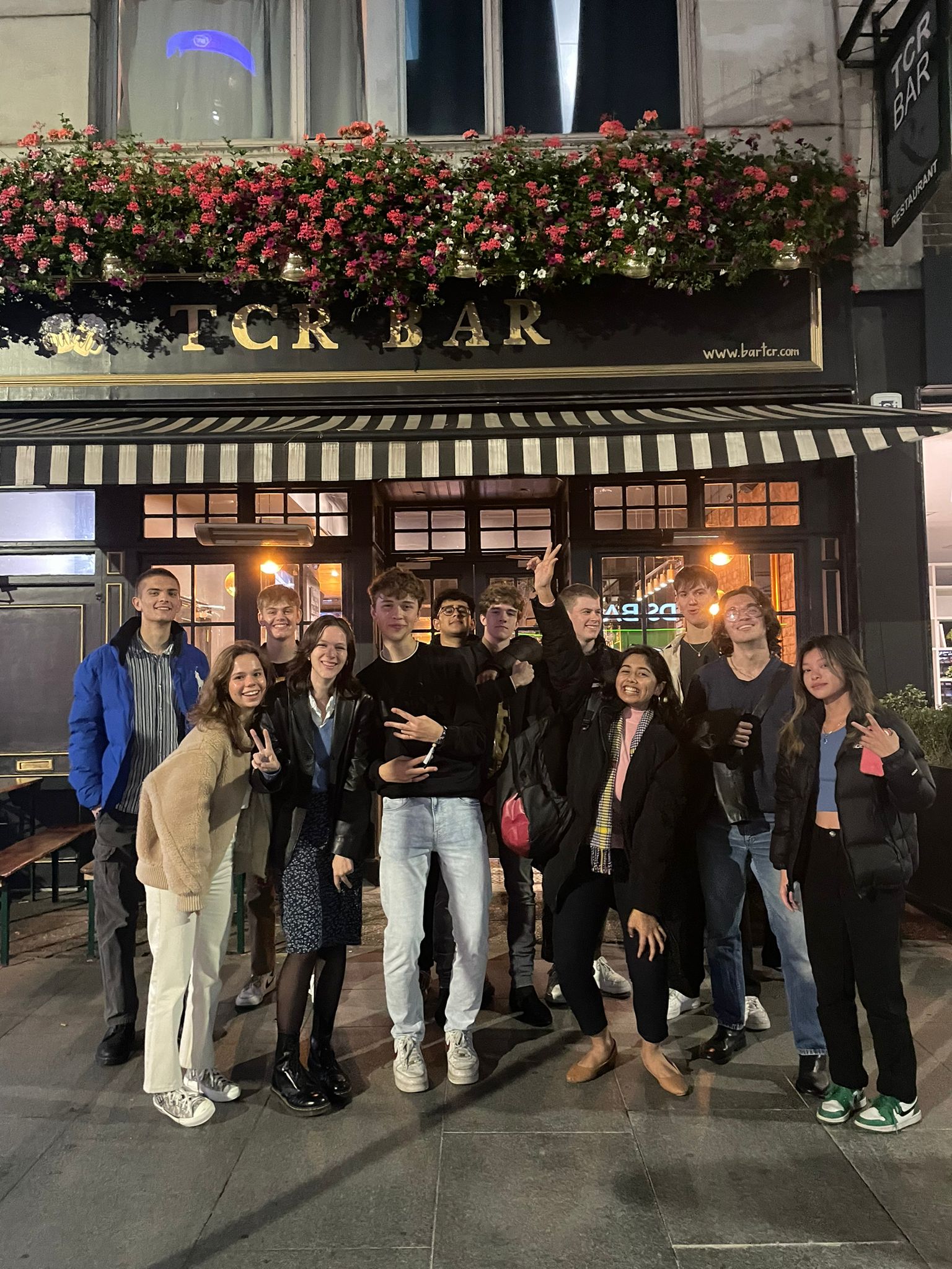 Image taken from EISPS Society's pub crawl, depicting twelve university-aged individuals standing outside the pub "TCR Bar" at night.
