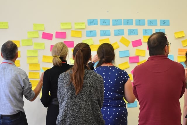 A group of people with their back toward the camera looking at a board with colourful sticky notes