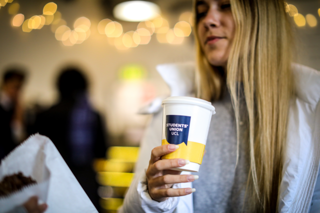 Female student holding a disposable coffee cup with Students Union branding