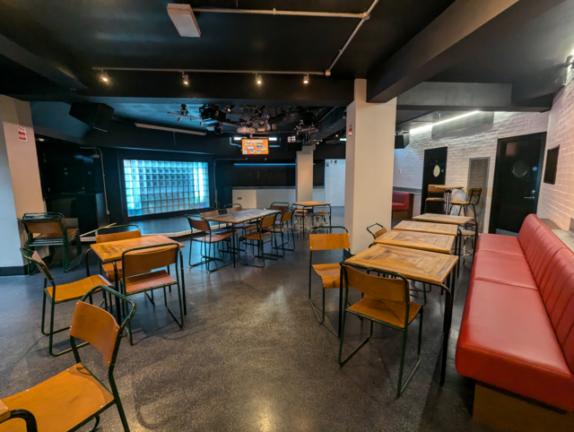 Photo of interior of Mullys showing a lit up stage, bench seating and tables and chairs around the bar