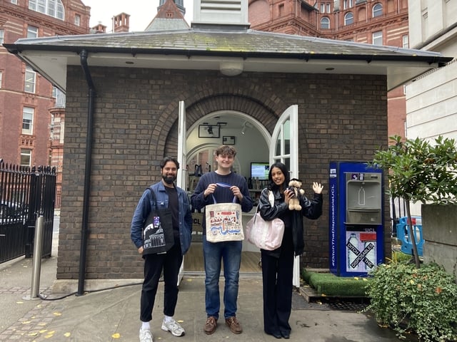 Three students holding UCL merch outside the North Lodge popup shop