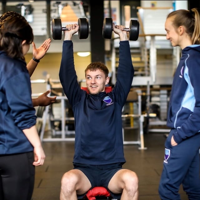 Student weightlifting with a staff member watching on offering support