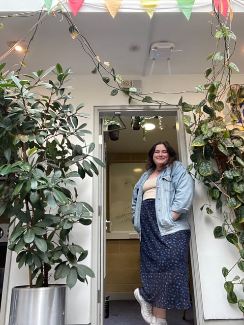 Photo of Molly standing in an office doorway, surrounded by plants and bunting, smiling into the camera