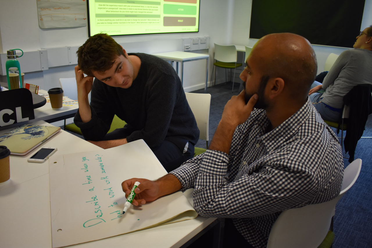 Two students talking whilst writing on flip chart