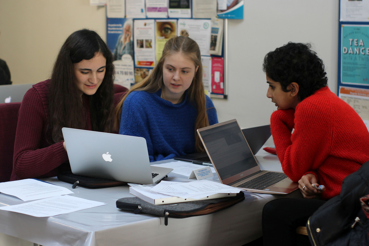 Three students working on laptops and talking